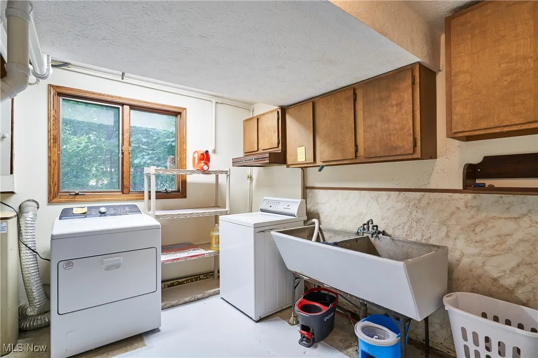 Washroom featuring cabinet space, washing machine and clothes dryer, a textured ceiling, and wainscoting