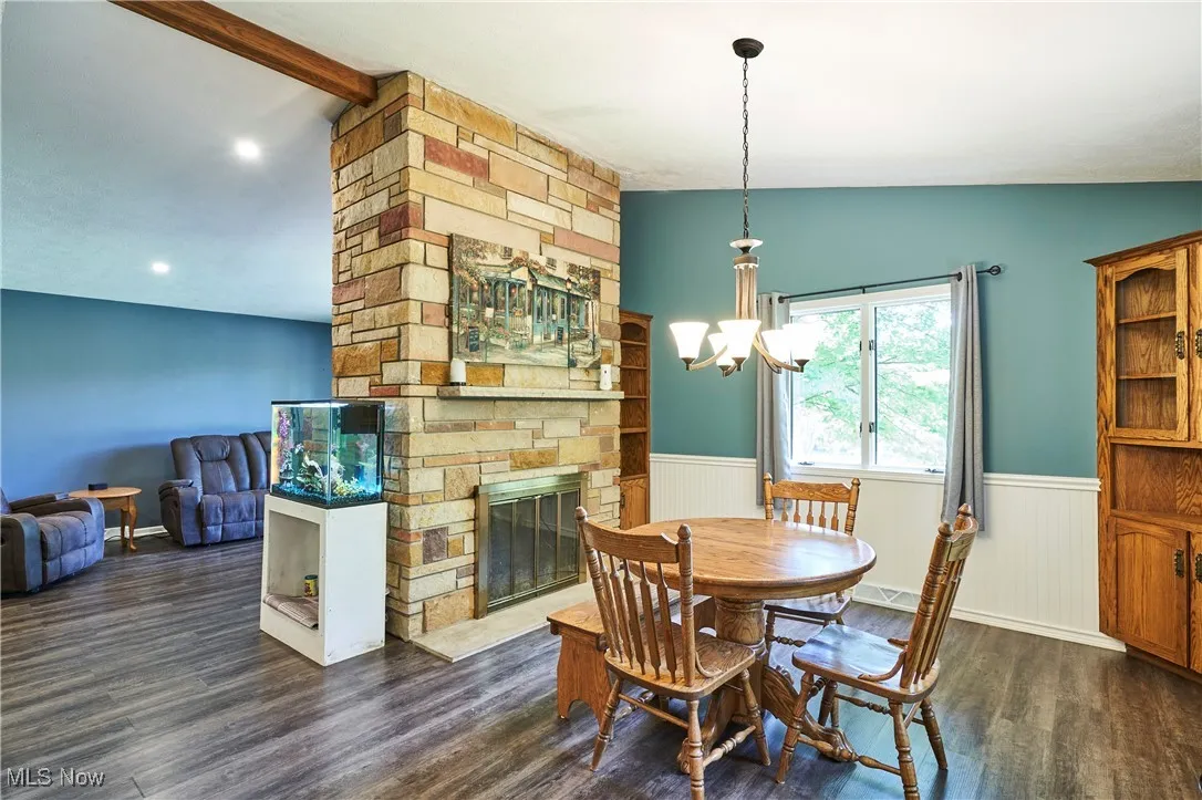 Dining area featuring lofted ceiling, a wainscoted wall, dark wood-type flooring, a chandelier, and a fireplace