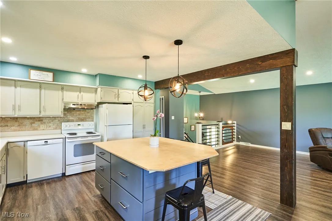 Kitchen with white appliances, beamed ceiling, open floor plan, tasteful backsplash, and dark wood-style flooring