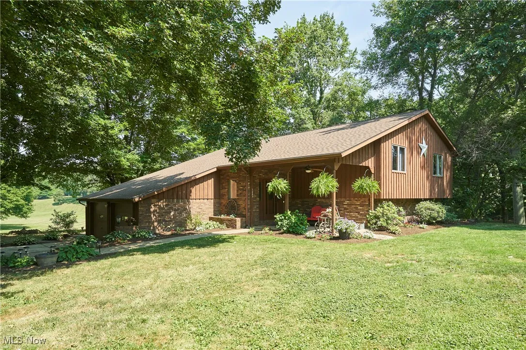 View of front of property with a front yard, board and batten siding, brick siding, and roof with shingles