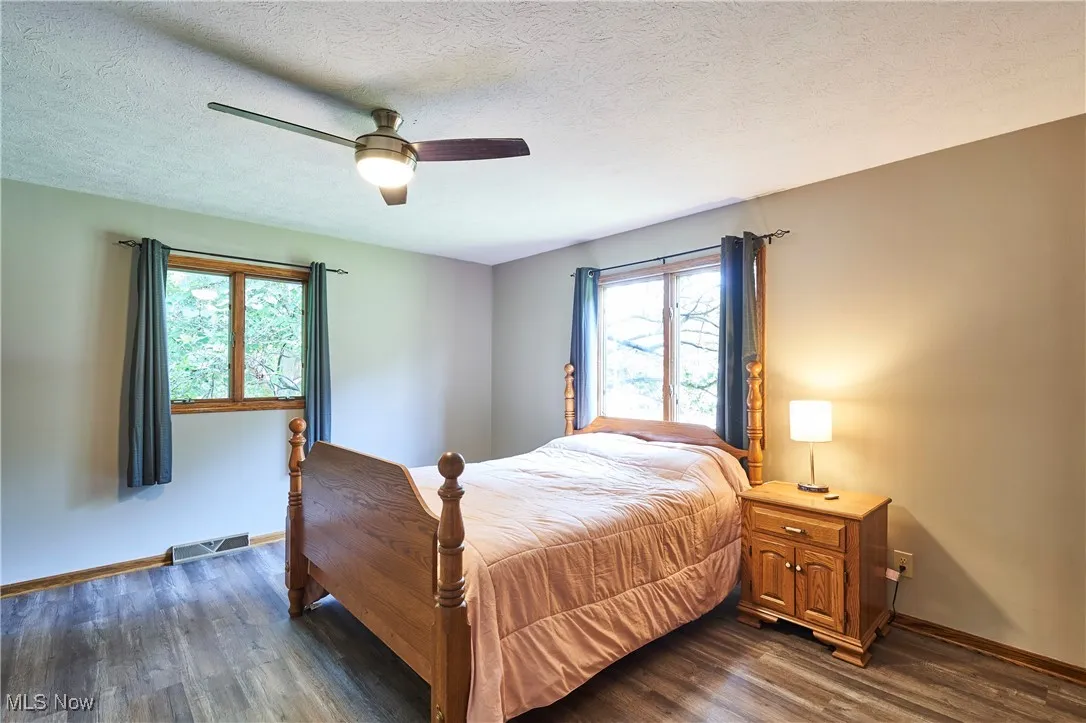 Bedroom featuring multiple windows, dark wood-style floors, a textured ceiling, and ceiling fan