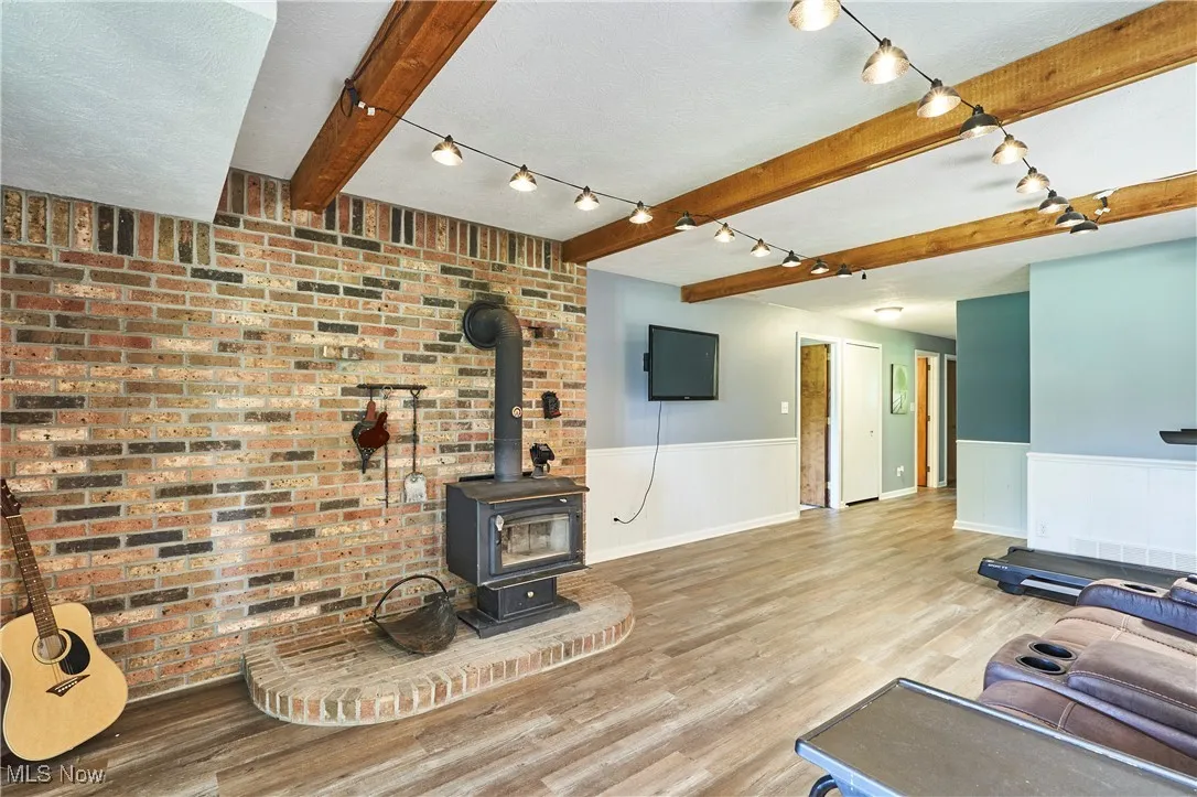 Living area with beam ceiling, a wainscoted wall, a wood stove, vinyl plank floors  and brick wall