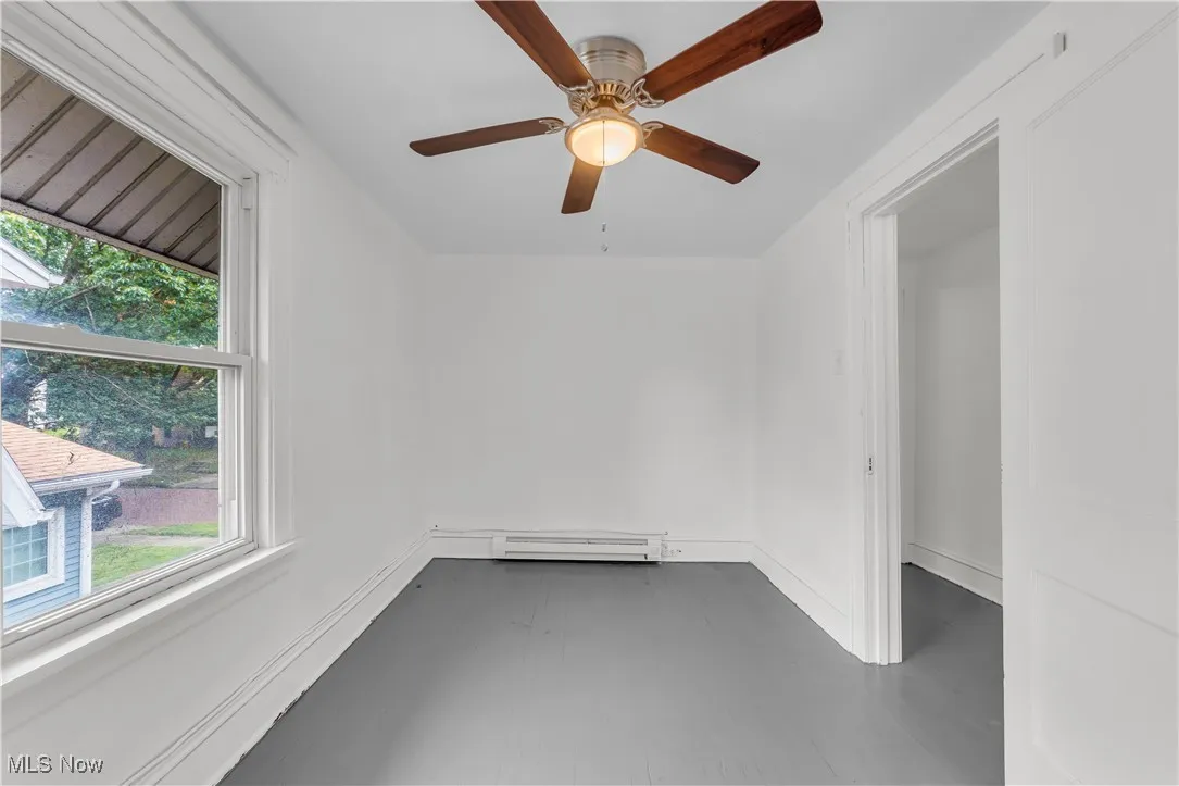 Unfurnished room featuring healthy amount of natural light, a baseboard heating unit, and ceiling fan