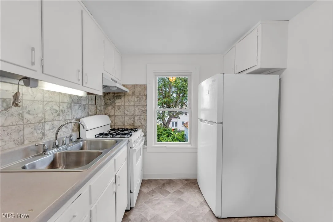 Kitchen featuring white appliances, white cabinets, under cabinet range hood, tasteful backsplash, and light countertops