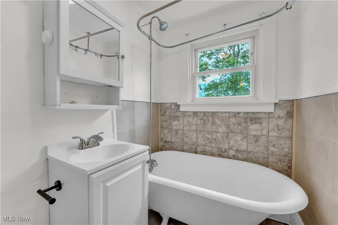 Full bathroom featuring a freestanding tub, vanity, tile walls, and a wainscoted wall