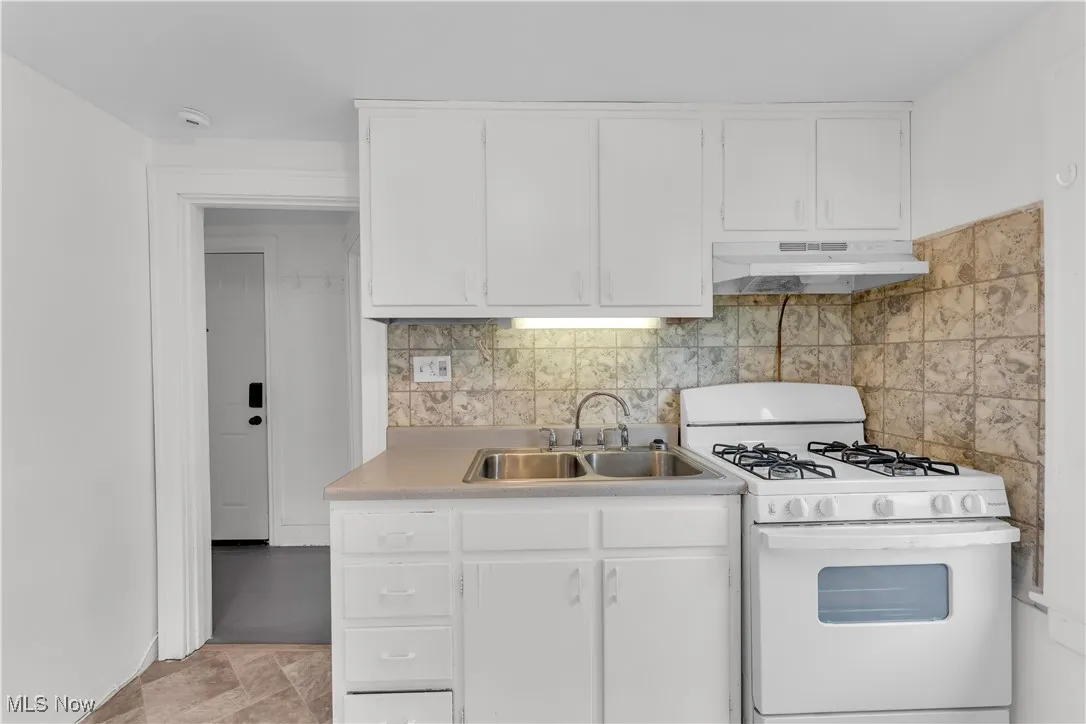 Kitchen with gas range gas stove, under cabinet range hood, light countertops, and white cabinetry