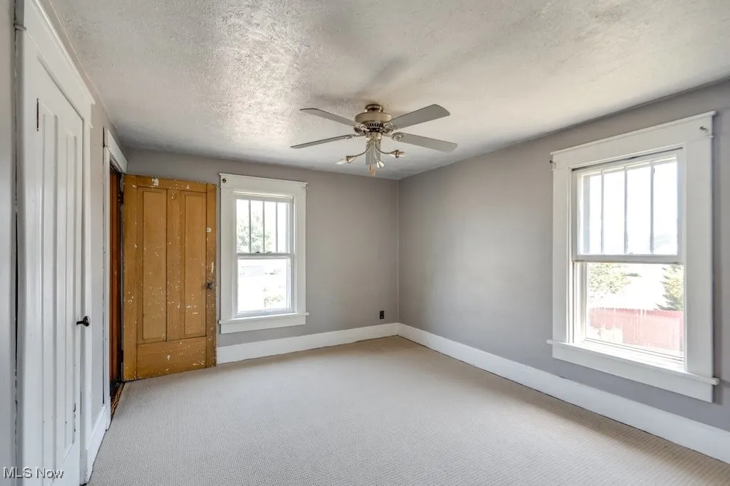 Unfurnished bedroom with light colored carpet, a textured ceiling, and a ceiling fan