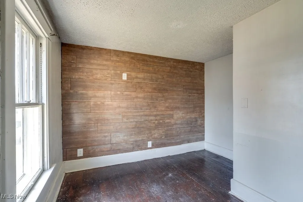 Unfurnished room featuring wood walls, plenty of natural light, a textured ceiling, wood-type flooring, and an accent wall