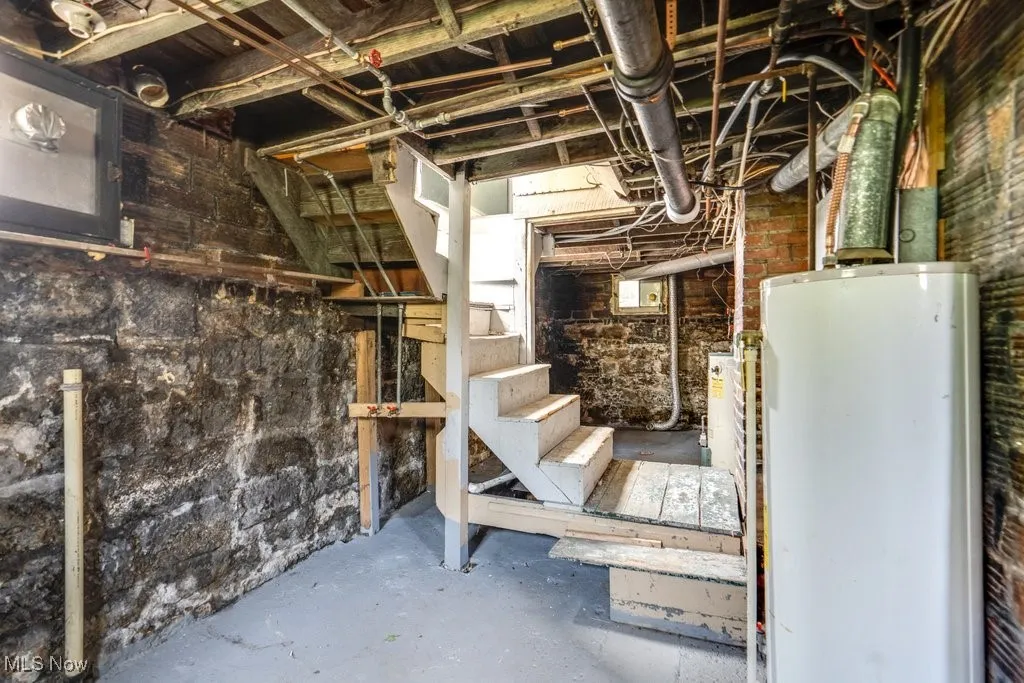 Unfinished below grade area featuring water heater and stairs