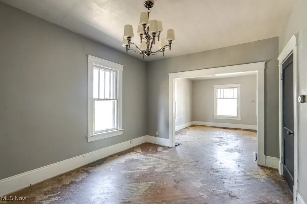 Unfurnished room with a chandelier and baseboards