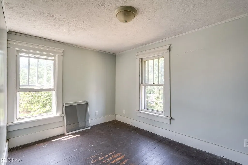 Empty room featuring wood-type flooring, plenty of natural light, a textured ceiling, and crown molding