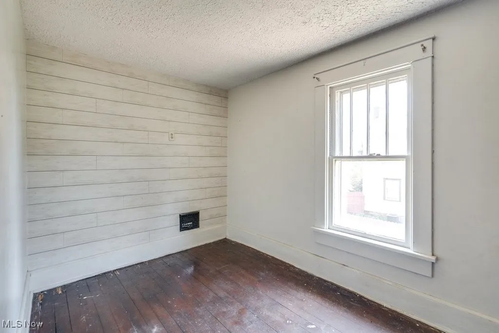 Unfurnished room with wood walls, dark wood-type flooring, a textured ceiling, and an accent wall