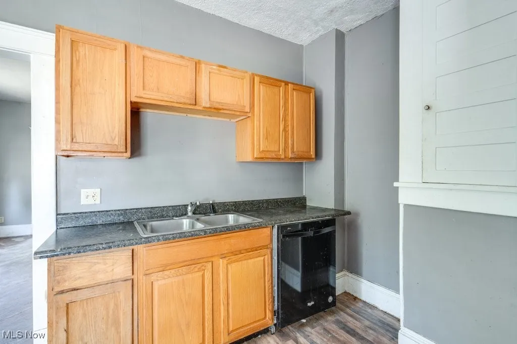 Kitchen featuring a textured ceiling, dark wood-style floors, black dishwasher, dark countertops, and light brown cabinets