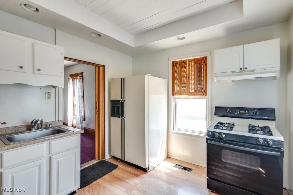 Kitchen featuring range with gas cooktop, white refrigerator with ice dispenser, light wood-type flooring, white cabinetry, and recessed lighting