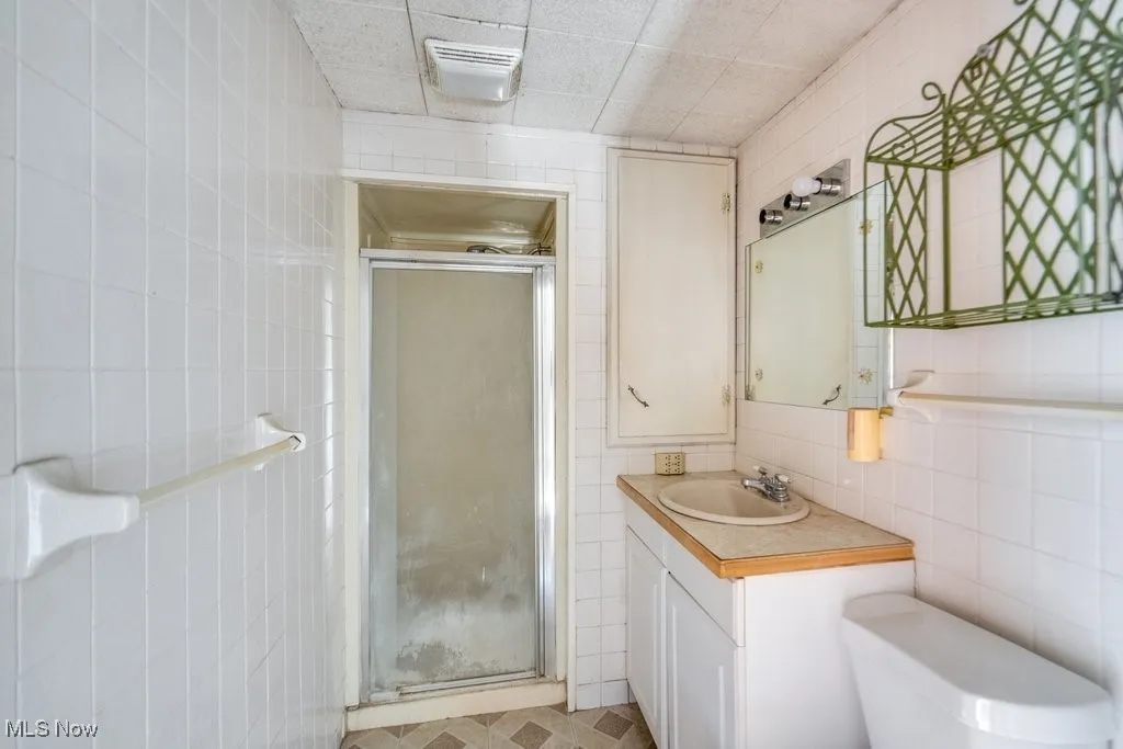 Bathroom featuring tile walls, a stall shower, and vanity