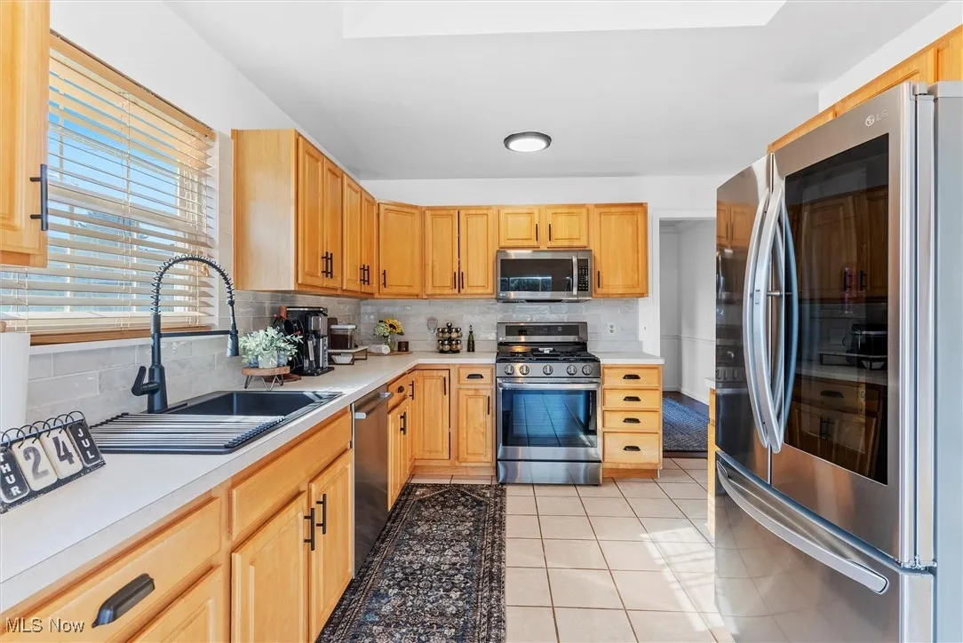 Kitchen featuring stainless steel appliances, light tile patterned floors, light countertops, and decorative backsplash