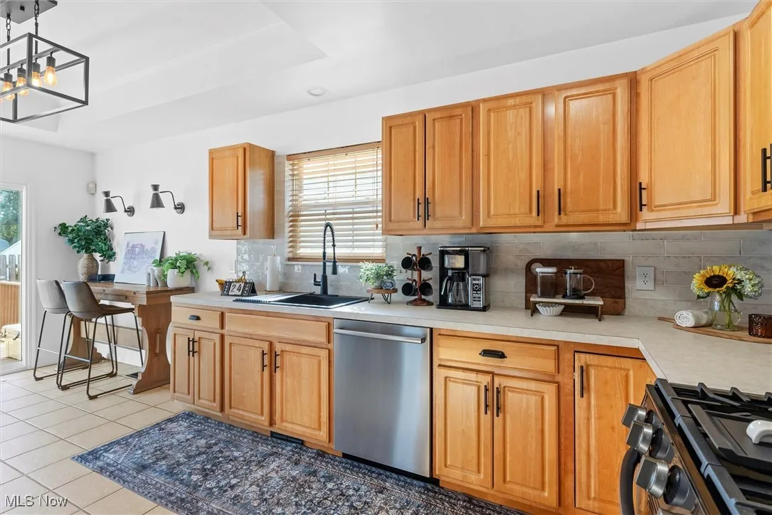 Kitchen with range with gas stovetop, stainless steel dishwasher, backsplash, light countertops, and light tile patterned floors