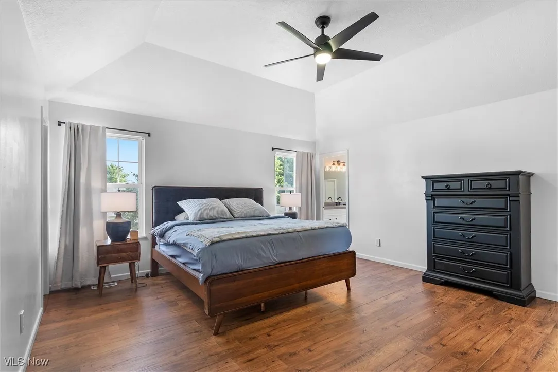 Bedroom featuring lofted ceiling, wood finished floors, a ceiling fan, and ensuite bathroom