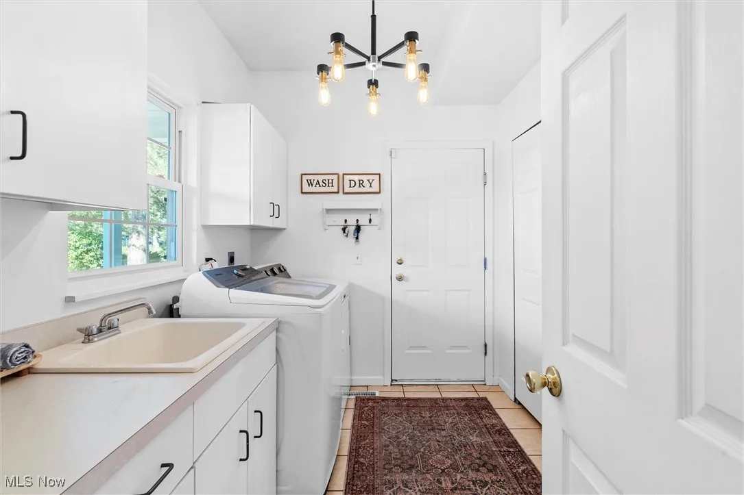 Laundry area featuring cabinet space, washer and clothes dryer, a chandelier, and light tile patterned floors