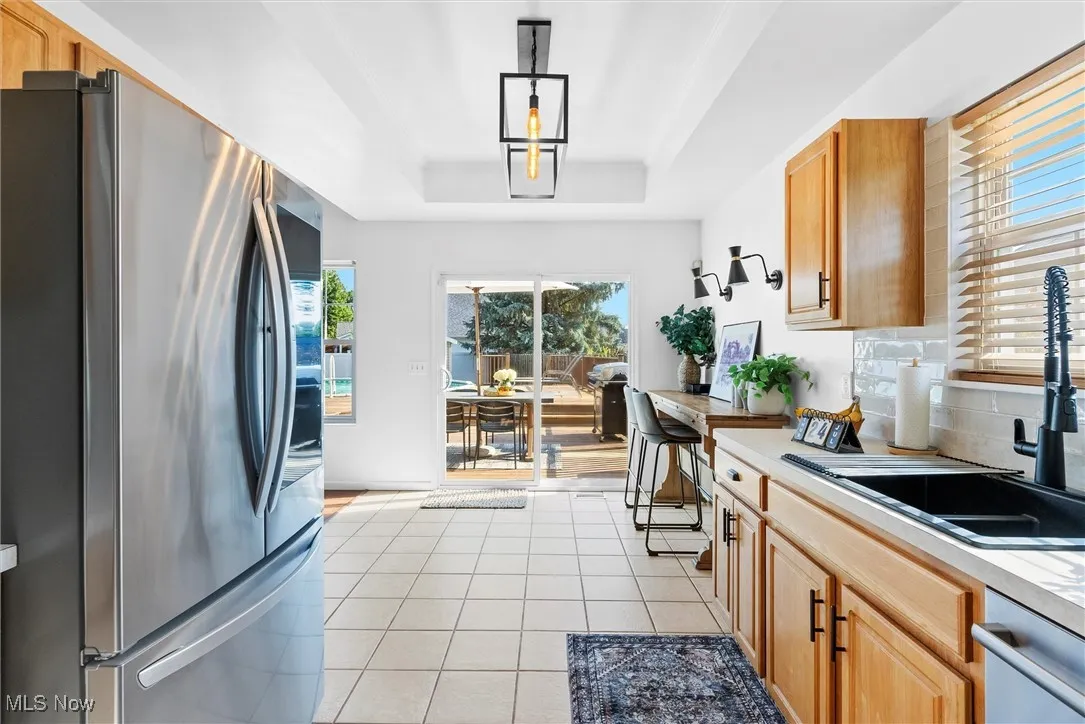 Kitchen with stainless steel appliances, a raised ceiling, light countertops, light tile patterned flooring, and tasteful backsplash