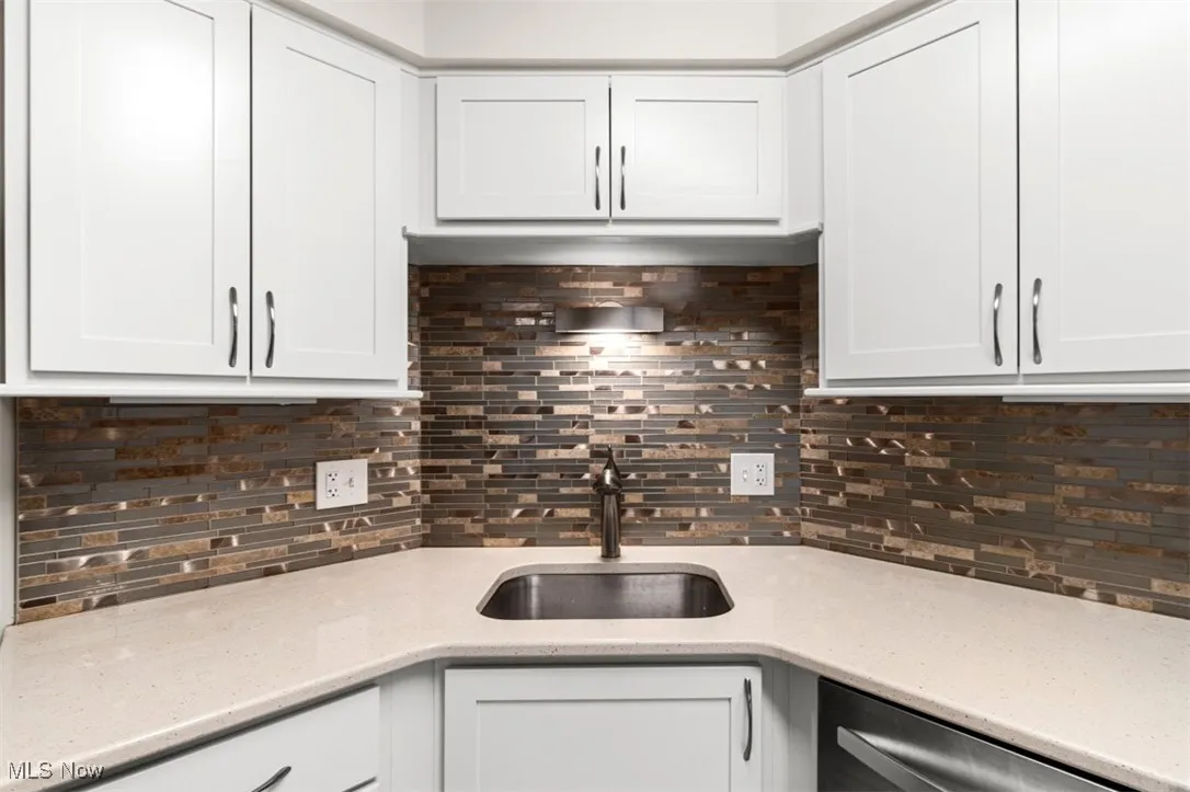 Kitchen featuring backsplash, white cabinetry, light stone counters, and stainless steel dishwasher