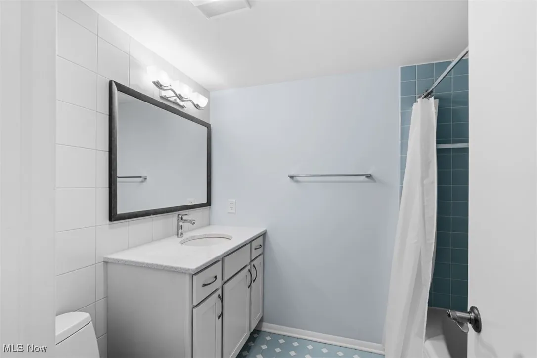 Bathroom with vanity, shower / tub combo with curtain, and tile walls
