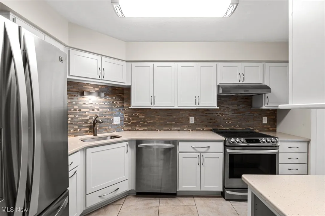 Kitchen featuring appliances with stainless steel finishes, decorative backsplash, light tile patterned flooring, white cabinets, and light stone countertops