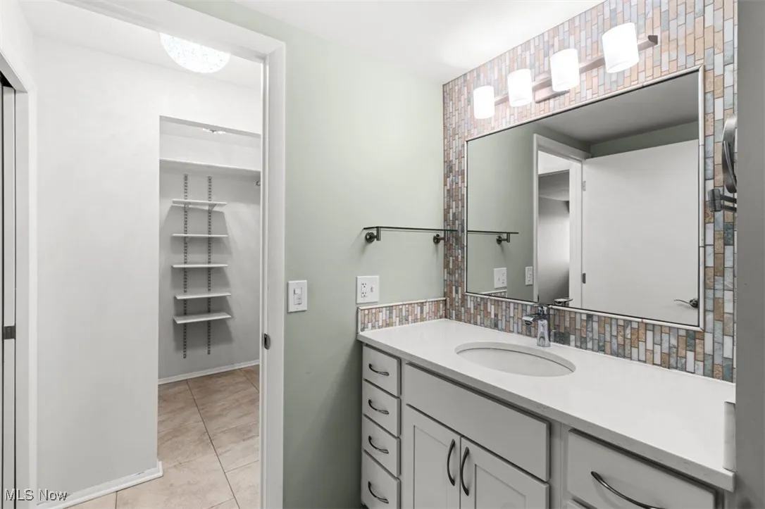 Bathroom featuring vanity, light tile patterned floors, decorative backsplash, and a walk in closet