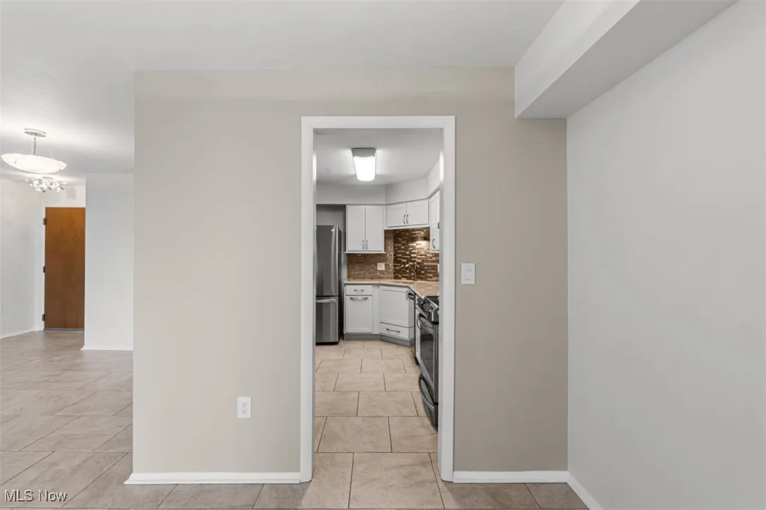 Kitchen with white cabinetry, tasteful backsplash, stainless steel appliances, light tile patterned flooring, and decorative light fixtures