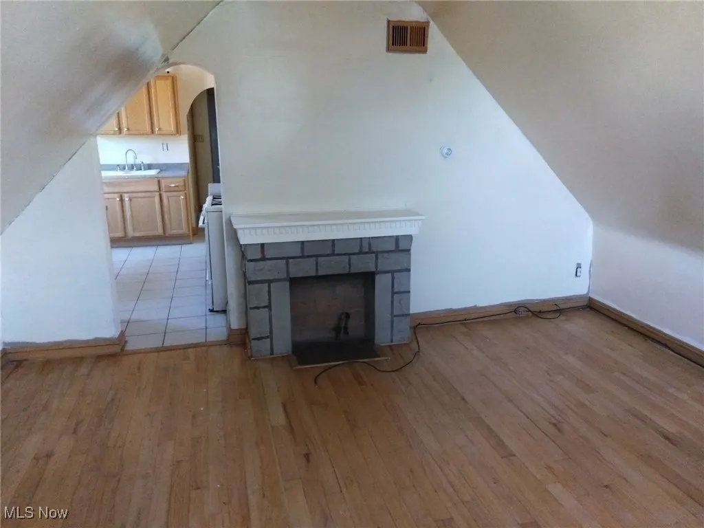 Bonus room featuring vaulted ceiling, light wood-style flooring, a fireplace, and arched walkways