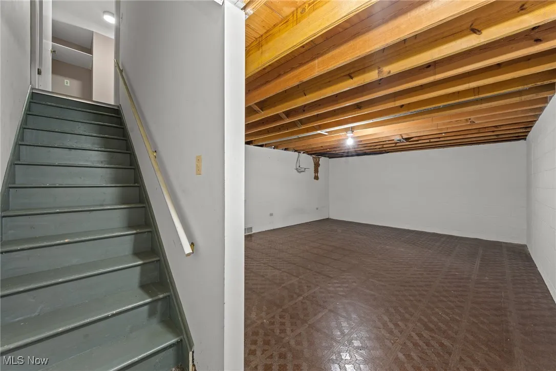 Finished basement with tile patterned floors, concrete block wall, and stairs
