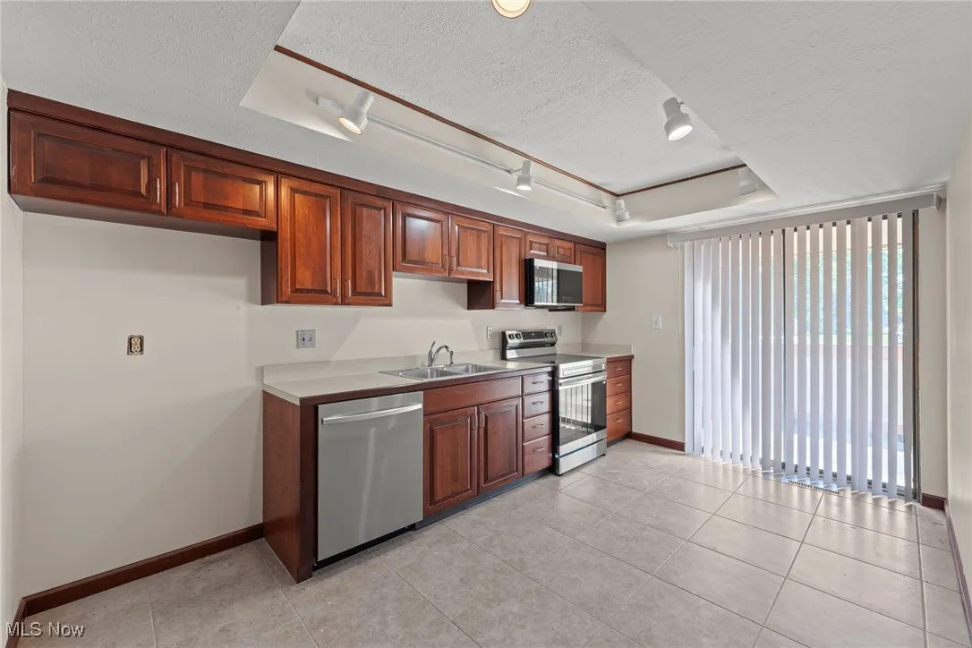 Kitchen featuring rail lighting, stainless steel appliances, a textured ceiling, light tile patterned floors, and light countertops