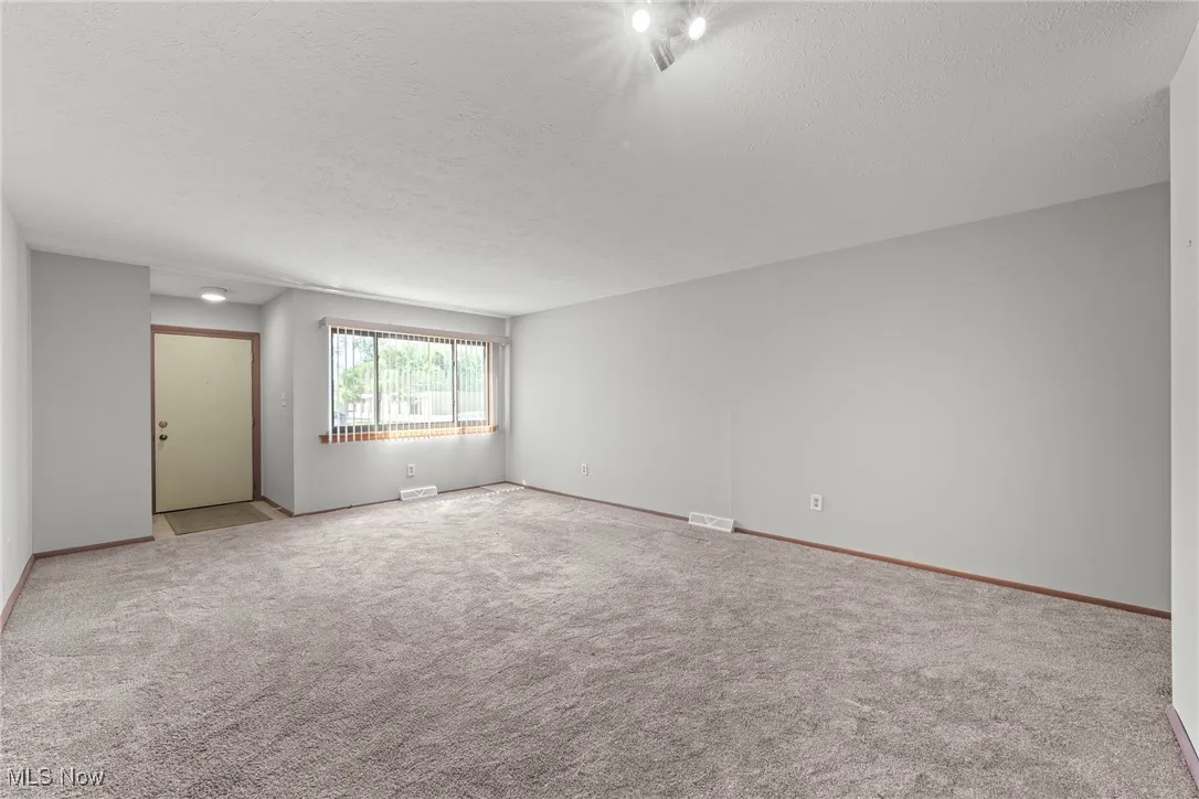 Carpeted spare room with a textured ceiling and baseboards