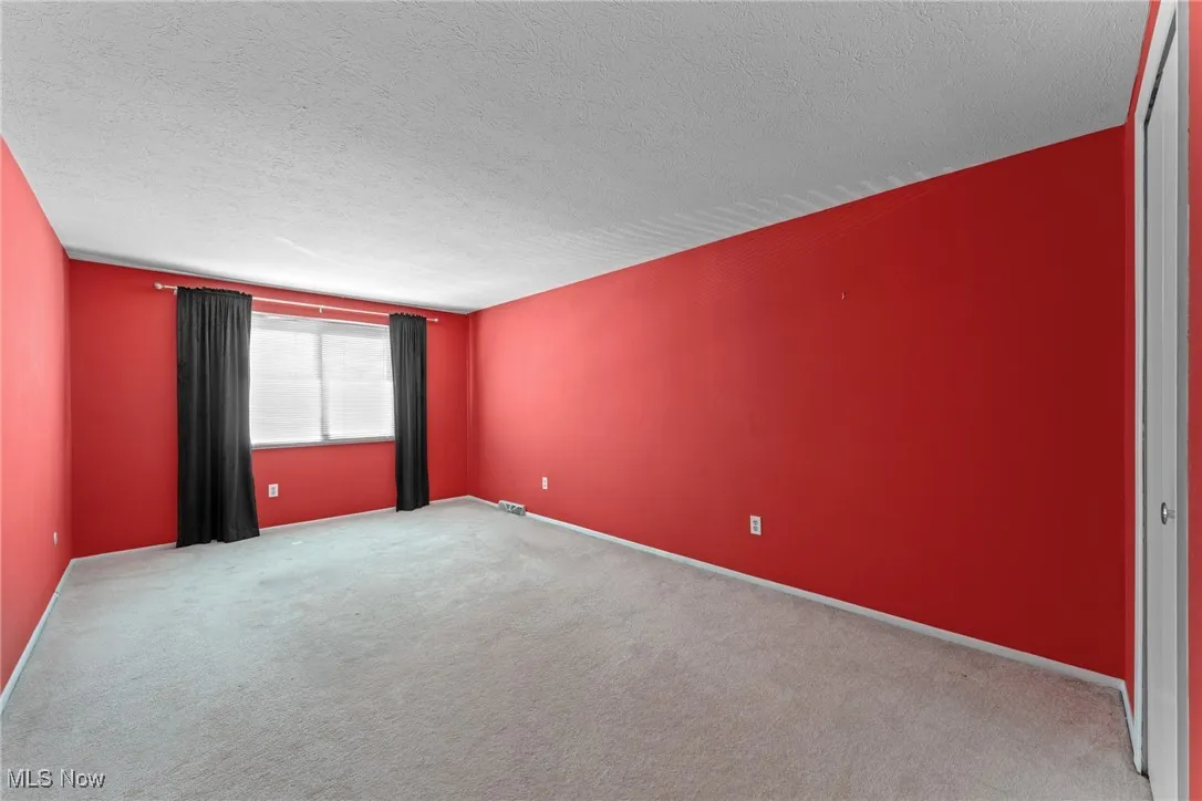 Carpeted empty room featuring a textured ceiling and baseboards