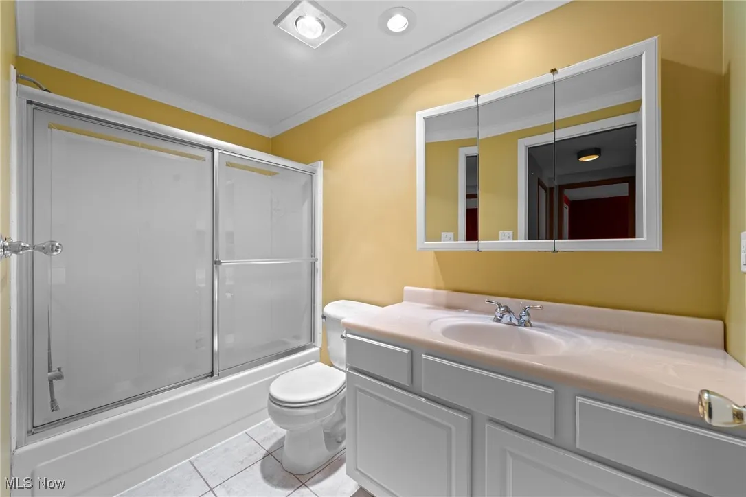 Bathroom with ornamental molding, vanity, enclosed tub / shower combo, and tile patterned flooring