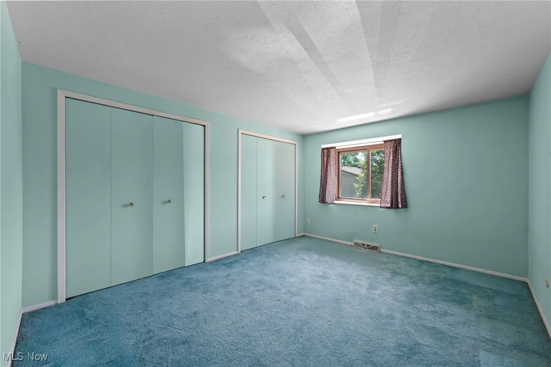 Unfurnished bedroom featuring multiple closets, carpet, and a textured ceiling