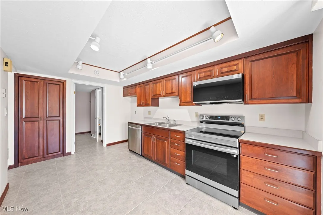 Kitchen with track lighting, stainless steel appliances, light countertops, light tile patterned floors, and brown cabinetry