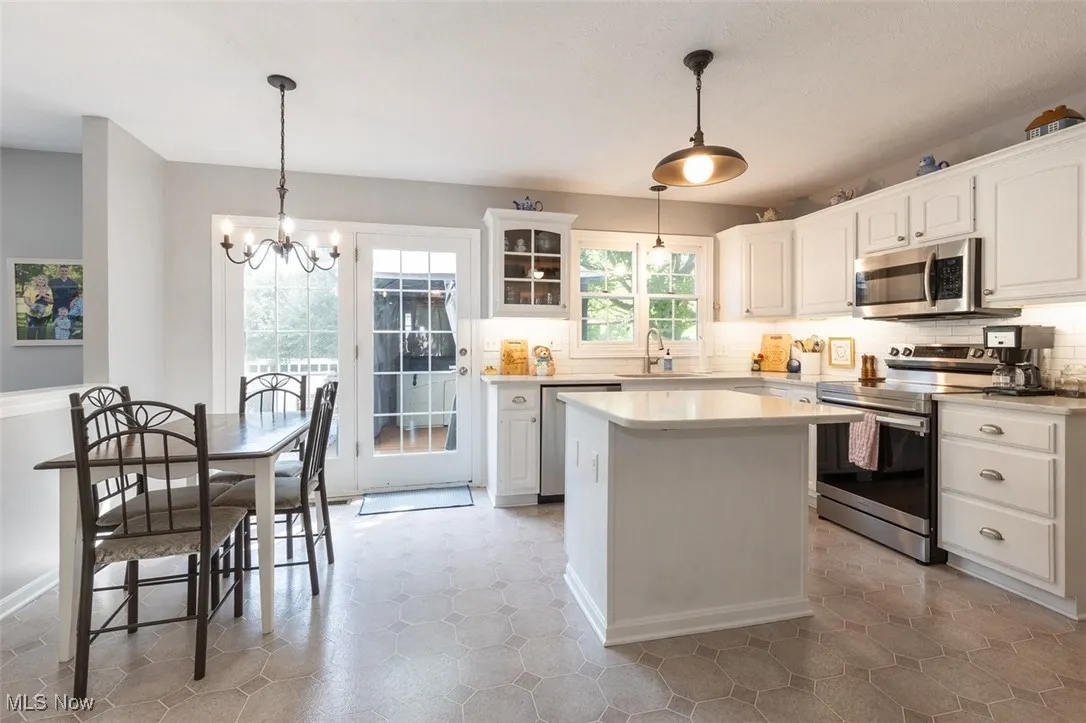 Kitchen featuring stainless steel appliances, a chandelier, a center island, white cabinets, and decorative backsplash