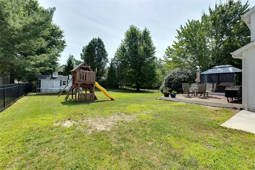 Fenced backyard with a playground, a trampoline, a gazebo, a wooden deck, and view of scattered trees