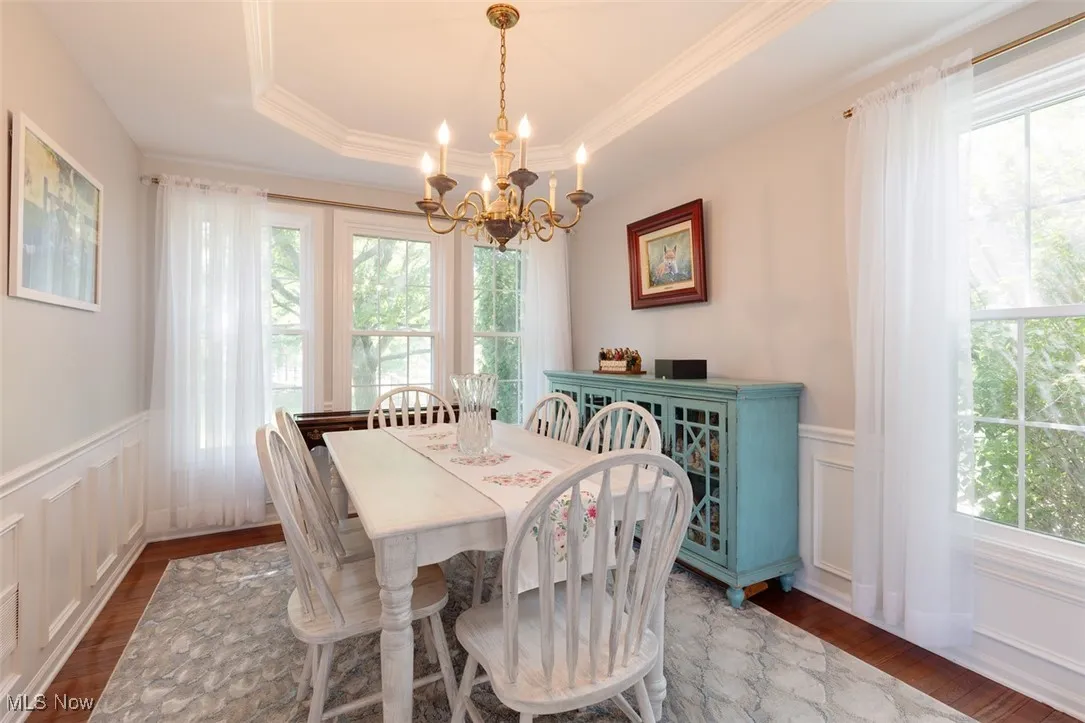 Dining area featuring a decorative wall, wainscoting, a chandelier, wood finished floors, and a raised ceiling
