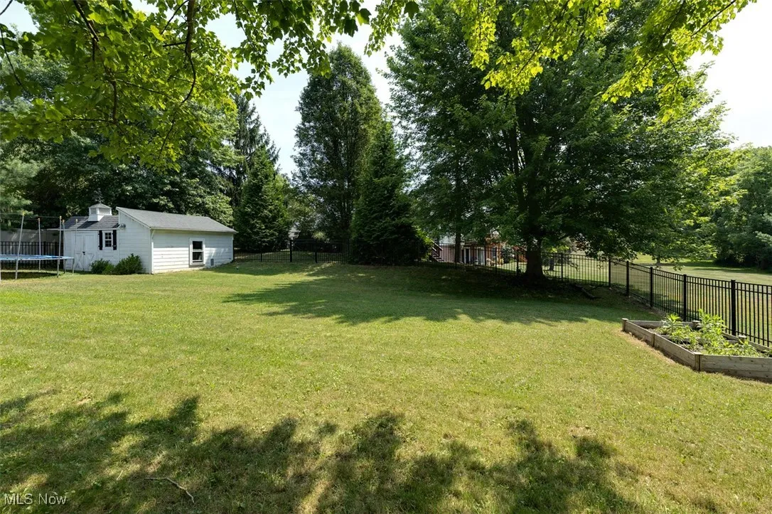 Fenced backyard with a trampoline, a vegetable garden, an outbuilding, and view of scattered trees