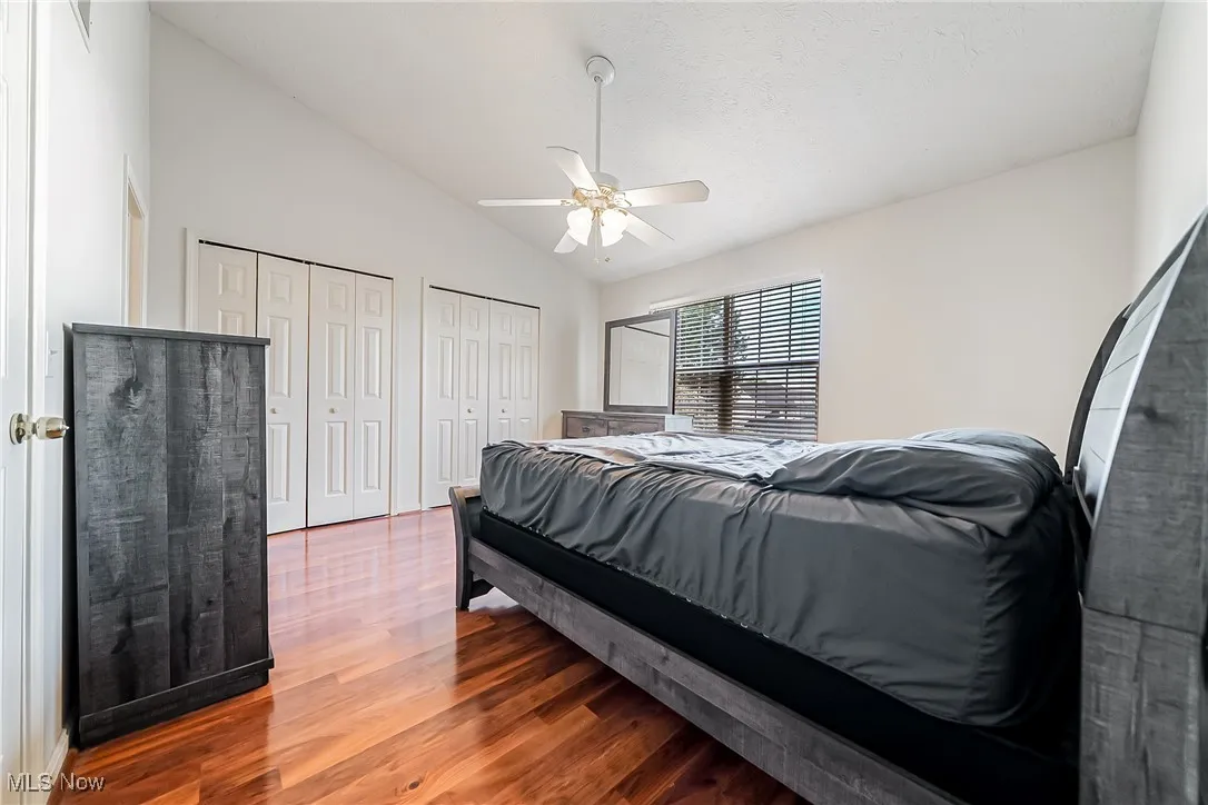 Bedroom featuring lofted ceiling, wood finished floors, two closets, and a ceiling fan