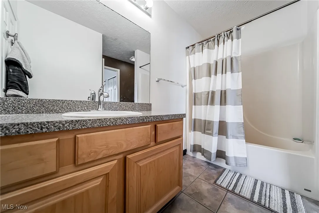 Bathroom featuring a textured ceiling, tile patterned flooring, vanity, and shower / bath combination with curtain