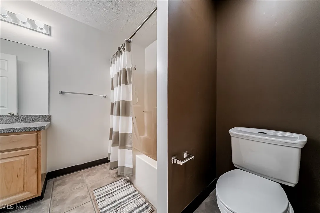 Full bath featuring a textured ceiling, vanity, tile patterned floors, and shower / tub combo with curtain