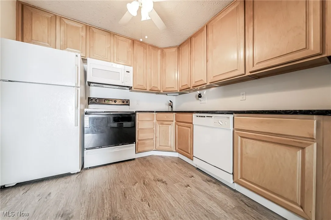 Kitchen featuring white appliances, light brown cabinetry, dark countertops, light wood-type flooring, and ceiling fan
