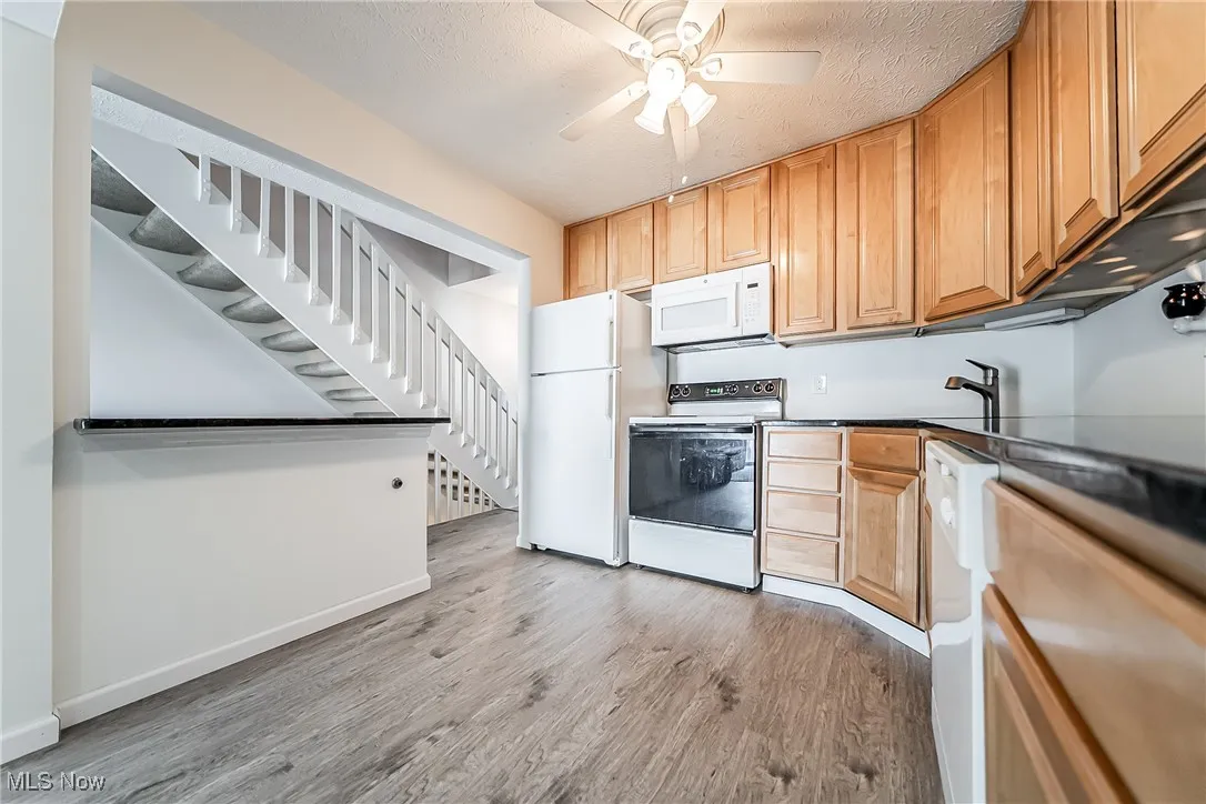 Kitchen with white appliances, light wood-type flooring, a textured ceiling, a ceiling fan, and dark countertops