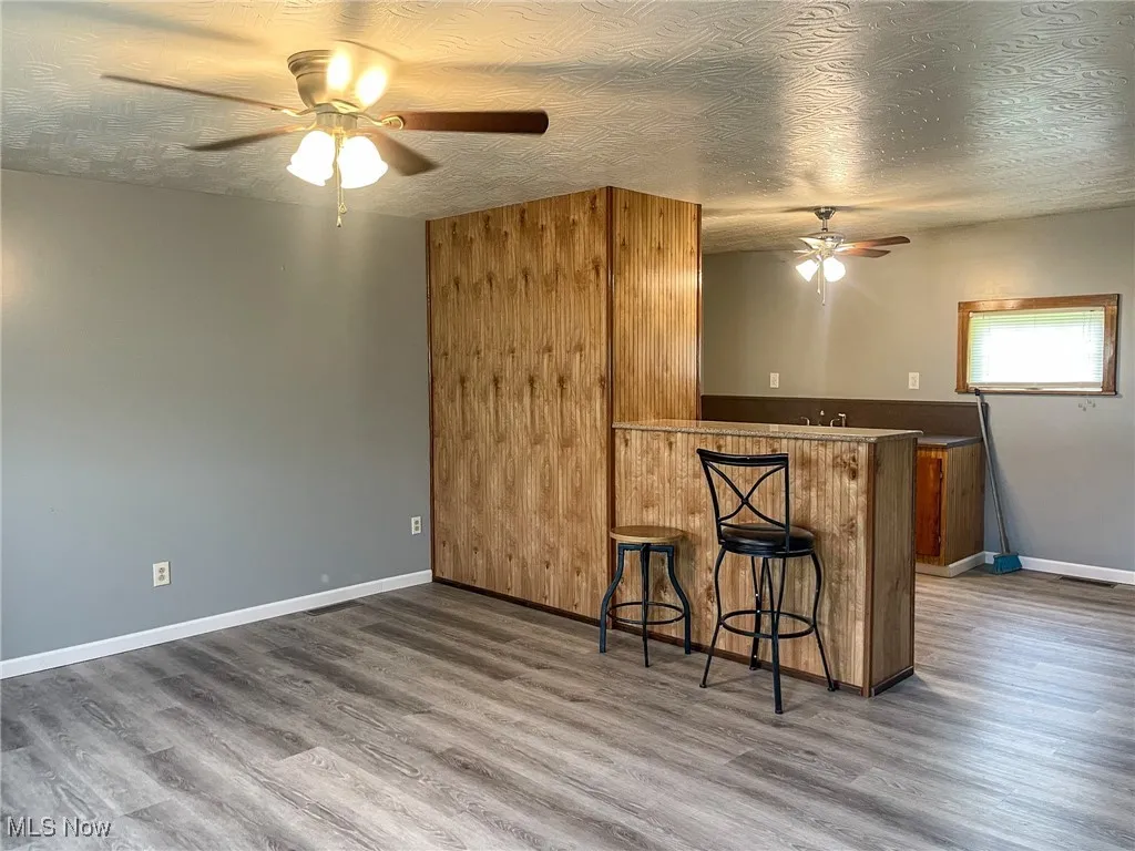 Kitchen with a ceiling fan, wood finished floors, a breakfast bar area, brown cabinets, and a peninsula