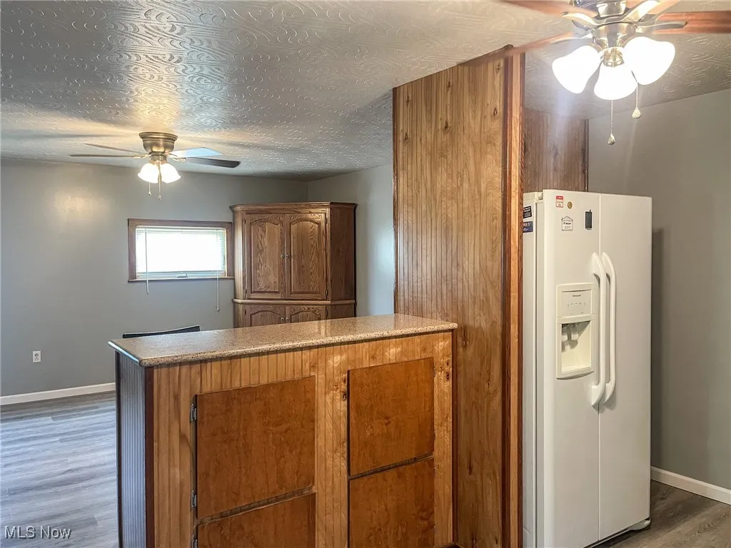 Kitchen with a ceiling fan, wood finished floors, white refrigerator with ice dispenser, a textured ceiling, and brown cabinetry