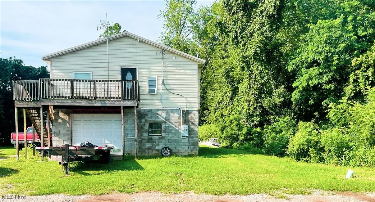 Rear view of property with a lawn, a garage, a deck, and stairs