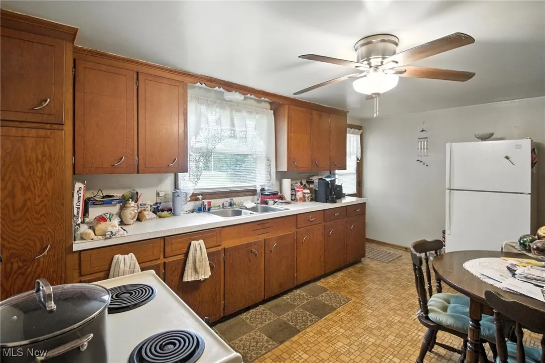 Kitchen featuring white appliances, brown cabinets, ceiling fan, and light countertops